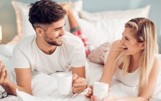 Couple enjoying coffee in bed while talking to each other.
