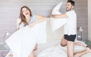 Man and woman having a pillow fight on a bed.