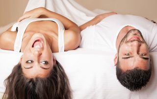 Man and woman in bed with their heads hanging off the mattress.