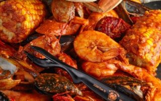 Image of boiled and seasoned crabs, corn, shrimp, and crawfish on a dark surface for Backyard Bayou.