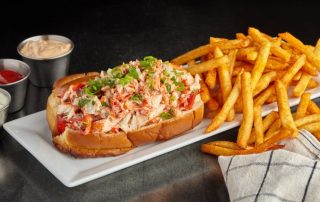 Lobster roll with a side of fries on a white plate.
